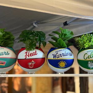 May include: Four basketball-themed planters, each with a team logo: San Antonio Spurs, Miami Heat, Golden State Warriors, and Boston Celtics. Each planter contains green plants, creating a unique decorative item for the home.