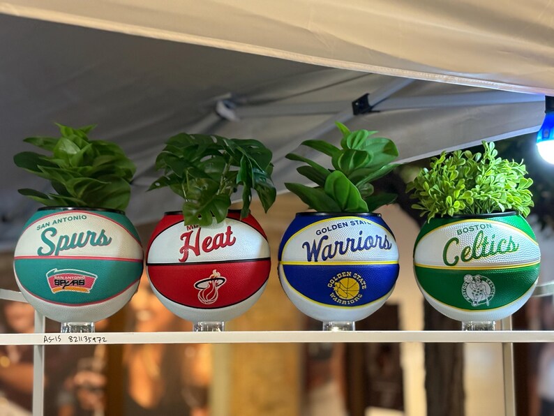 May include: Four basketball-themed planters, each with a team logo: San Antonio Spurs, Miami Heat, Golden State Warriors, and Boston Celtics. Each planter contains green plants, creating a unique decorative item for the home.