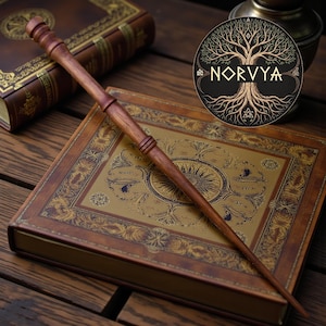 May include: A wooden wand with a tapered design, lying on a leather-bound book with gold embossed details. The wand is a rich brown colour. A circular emblem with the word "NORVYA" and a tree design is in the background.