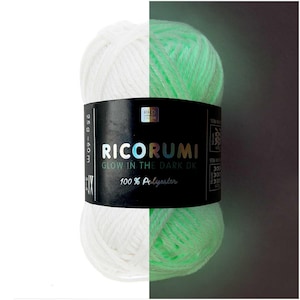 May include: A ball of Ricorumi Glow in the Dark DK yarn made of 100% polyester. The label indicates 25g and 60m. The yarn appears white on the left side and glows with a light green hue on the right side, demonstrating its light-emitting property.