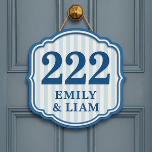 May include: A blue and white striped house number sign with the number "222" in dark blue. The sign also displays the names "EMILY & LIAM" in a serif font. The sign is hanging on a blue door.