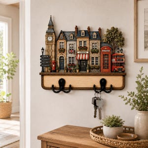 May include: A wall-mounted key holder featuring a three-dimensional London street scene with Big Ben, a red telephone booth, and a double-decker bus. The wooden base includes two black metal double hooks, with a set of keys hanging from one hook.