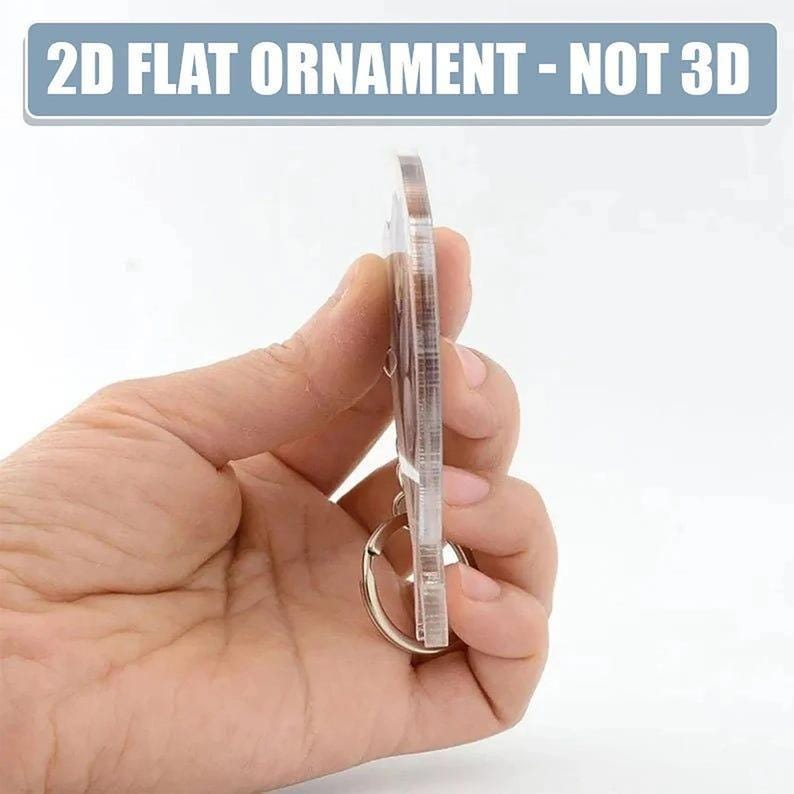 A hand holding a clear plastic ornament, which appears to be a 2D flat ornament.