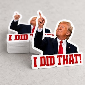 May include: White stickers featuring a smiling man in a suit and red tie, pointing upwards. The text "I DID THAT!" is in red block letters. A stack of similar stickers is visible.