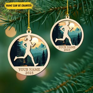 May include: Two wooden running-themed ornaments hanging from a Christmas tree. Each ornament features a silhouette of a runner in front of a mountain and forest scene. The text "YOUR NAME 2025" is printed on the bottom of each ornament.
