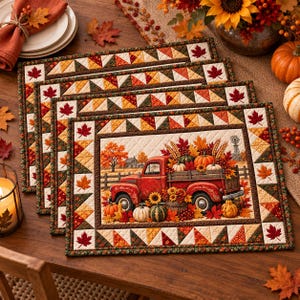 May include: A set of four rectangular quilted placemats featuring a central illustration of a red vintage pickup truck loaded with pumpkins, sunflowers, and autumn leaves, surrounded by a border of geometric triangles and maple leaf motifs.