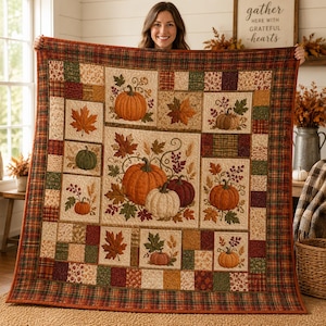 May include: A patchwork quilt featuring a seasonal autumn theme with various blocks displaying printed pumpkins, fall leaves, and berries in shades of orange, green, brown, and cream. The quilt is bordered by a plaid fabric in matching fall colors.