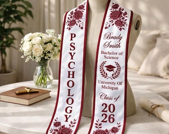 May include: White graduation sash with maroon trim and floral accents. The sash displays the word "PSYCHOLOGY" vertically, and the name "Brady Smith", "Bachelor of Science", "University of Michigan", and "Class of 2026".