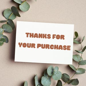 A white card with the text "THANKS FOR YOUR PURCHASE" written on it, surrounded by green leaves and branches.