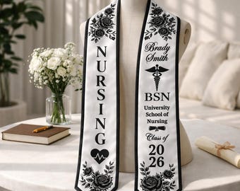 May include: White graduation sash with black trim and floral rose accents. The sash features the word "NURSING" in large black letters, a heart with a heartbeat, and the name "Brady Smith" with "BSN" and "Class of 2026".