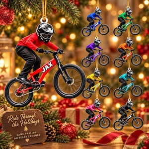 May include: A collection of Christmas ornaments featuring a cyclist wearing a helmet and riding a bicycle with the name JAX on the frame. The ornaments come in various colors including red, blue, green, purple, orange, yellow, teal, pink, and black.