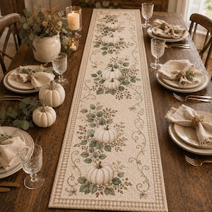 May include: A long, rectangular quilted table runner featuring a repeating pattern of white pumpkins, green leaves, and brown vines on a cream background, bordered by a tan and white checkered trim, displayed on a dark wooden dining table.