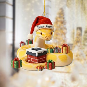 May include: A yellow snake Christmas ornament wearing a red Santa hat with the text "Your Name". The ornament is surrounded by wrapped gift boxes and a brick chimney. A festive holiday decoration.