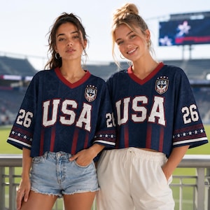 Two young women wearing matching USA jerseys pose together in front of a stadium.