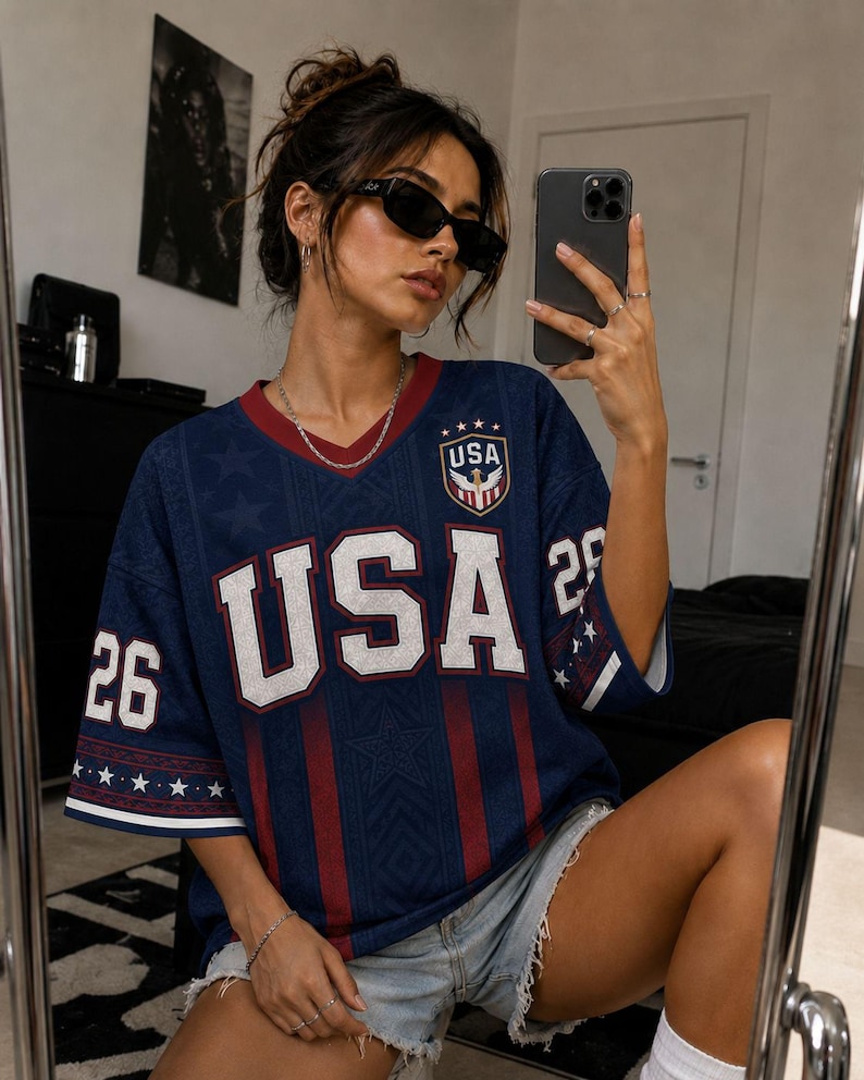 A woman wearing a blue USA jersey with the number 26 is taking a selfie in front of a mirror.