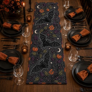 May include: A rectangular table runner featuring a dark gray quilted fabric with a repeating pattern of black bats, orange pumpkins, crescent moons, and colorful floral vines, finished with a thin orange and black checkered border trim.