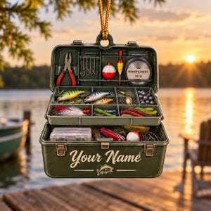 May include: An olive green hanging ornament shaped like an open fishing tackle box. The box contains pliers, hooks, a red and white bobber, and a spool labeled MONOFILAMENT 12 LB. The front features the text Your Name and a fish graphic.