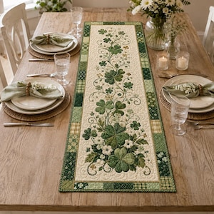 May include: A rectangular quilted table runner featuring a central cream-colored panel decorated with green shamrock and clover motifs, surrounded by a patchwork border of various green and white patterned fabric squares.