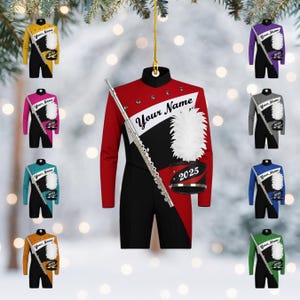 May include: Ornament featuring a red, black, and white marching band uniform with the text "Your Name" and "2025". A silver flute and a white plume hat are also included. Additional ornaments in various colors are visible.