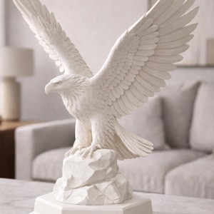 May include: A white ceramic eagle sculpture with outstretched wings, perched atop a rock-like base. The eagle is detailed with textured feathers and stands on a geometric pedestal. This decorative piece is ideal for home decor.
