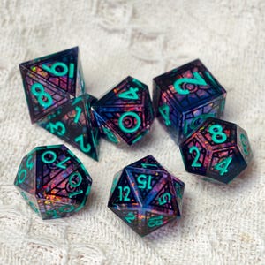 May include: A set of seven polyhedral dice featuring a dark, translucent resin base with embedded iridescent, multi-colored foil flakes and a black geometric grid pattern. Each die has bright teal, raised numerals for clear visibility.