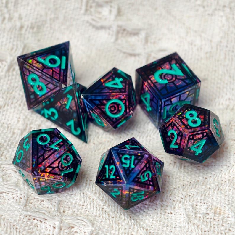May include: A set of seven polyhedral dice featuring a dark, translucent resin base with embedded iridescent, multi-colored foil flakes and a black geometric grid pattern. Each die has bright teal, raised numerals for clear visibility.