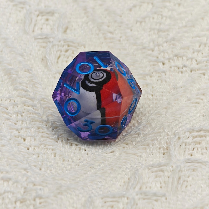 May include: A purple and blue 12-sided die with a Pokemon character inside. The die has numbers 1-12 on the sides.