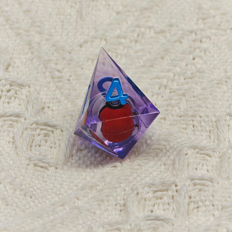 May include: A purple, clear, triangular dice with a red sphere inside and the number "4" printed on one side.