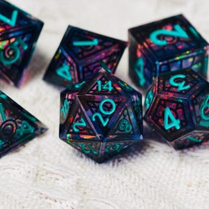 Può includere: Un set di dadi poliedrici caratterizzati da una base in resina scura e traslucida con scaglie iridescenti incastonate che brillano nei toni del viola e del blu. Ogni dado presenta una struttura geometrica nera e numeri incisi color ottanio.