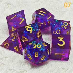 Puede incluir: Conjunto de siete dados de color p&uacute;rpura iridiscente con n&uacute;meros dorados. Los dados est&aacute;n hechos de un material transparente con un acabado brillante. Los n&uacute;meros en los dados son 3, 4, 6, 8, 10, 12 y 20.