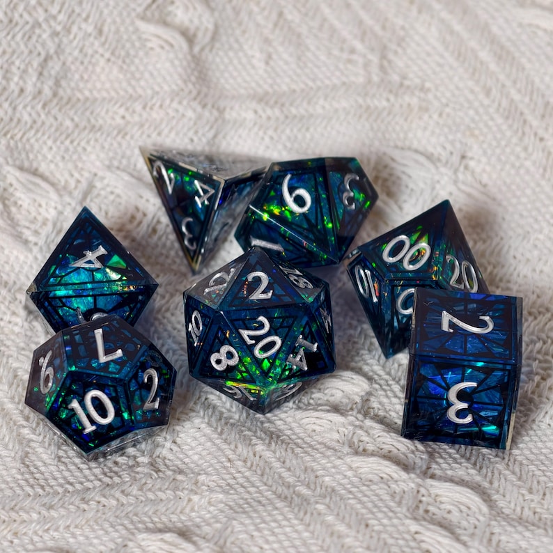 May include: A set of seven polyhedral dice featuring a dark blue and green translucent resin base with embedded iridescent foil shards and crisp white numerals. The collection includes a d20, d12, d10, d8, d6, d4, and a percentile die.