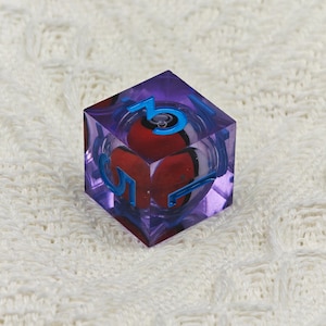 May include: A purple, clear, six-sided dice with blue numbers. The dice has a red and white sphere inside.