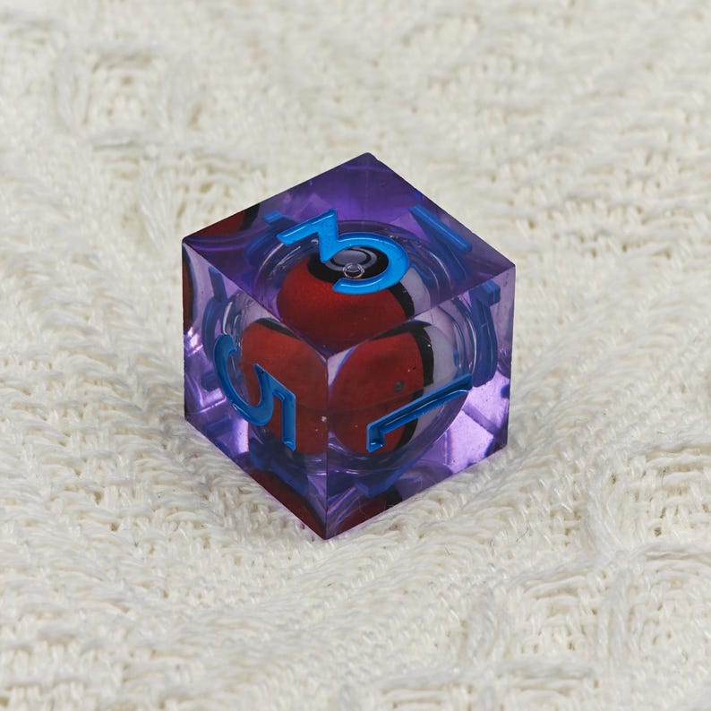 May include: A purple, clear, six-sided dice with blue numbers. The dice has a red and white sphere inside.