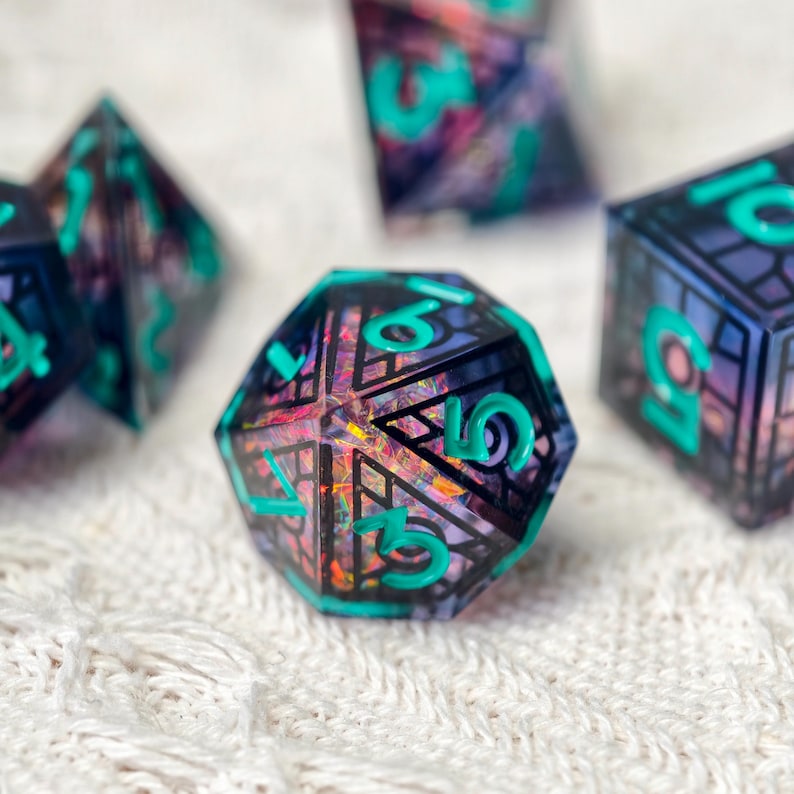 May include: A set of polyhedral dice featuring a dark, translucent resin base with an intricate black geometric grid pattern and embedded iridescent foil flakes. The numbers are engraved and filled with a bright, opaque teal pigment.
