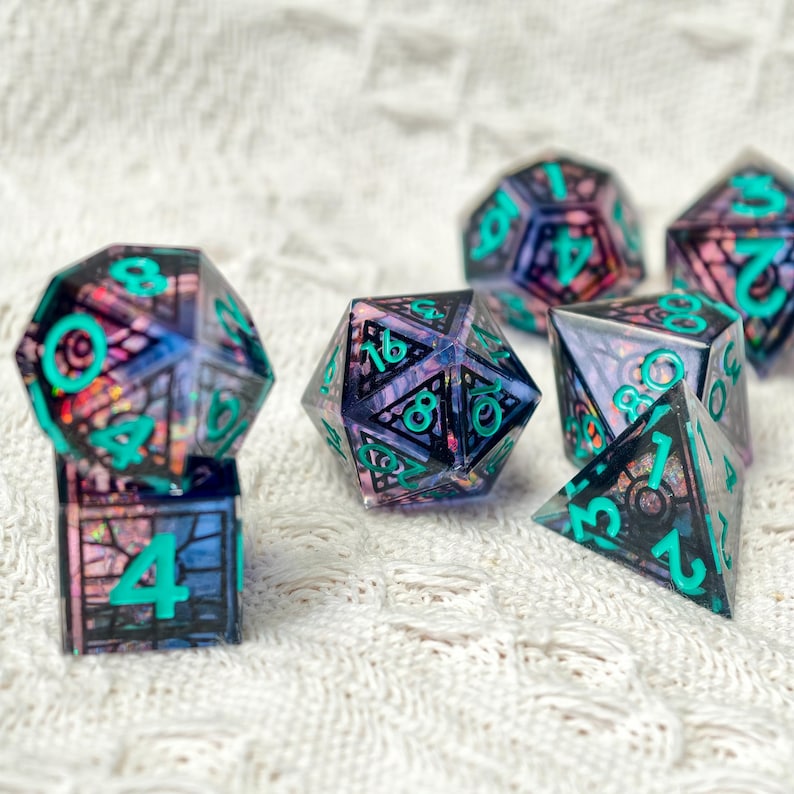 May include: A set of polyhedral dice featuring a translucent purple and black stained glass pattern with iridescent glitter inclusions. Each die has bold, bright teal numbers etched into the surface, including a d20, d12, d10, d8, d6, and d4.