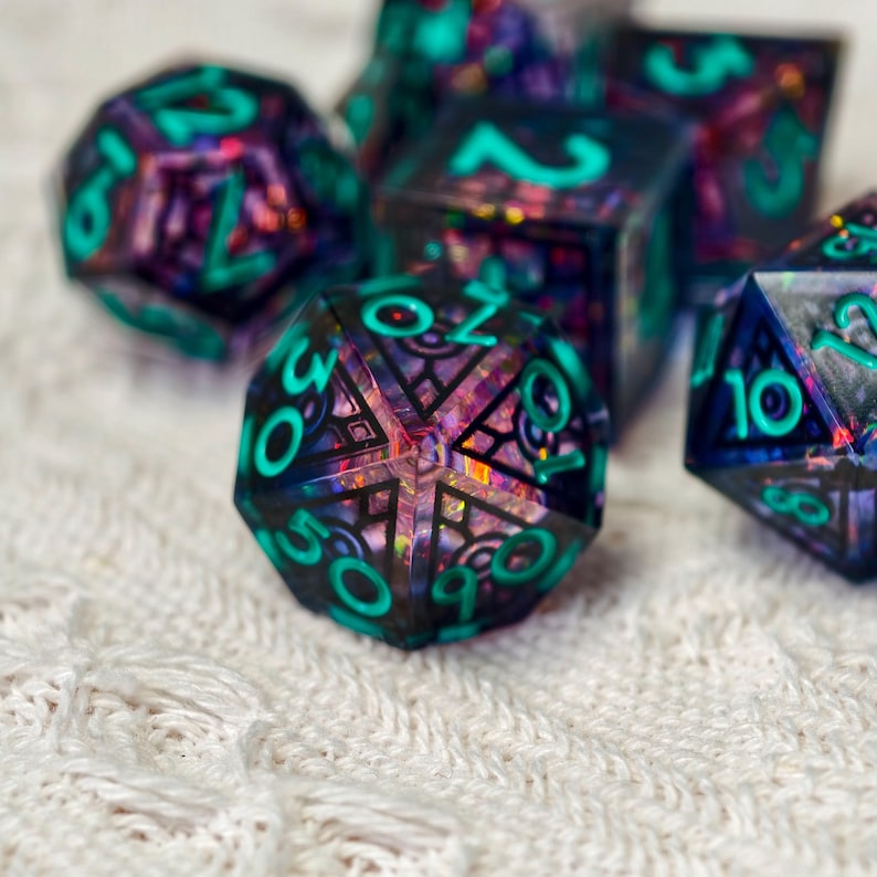 May include: A set of multi-faceted polyhedral dice featuring a dark, translucent resin base with embedded iridescent glitter and bold, bright teal numbers. The dice display intricate geometric patterns visible through the clear, dark material.