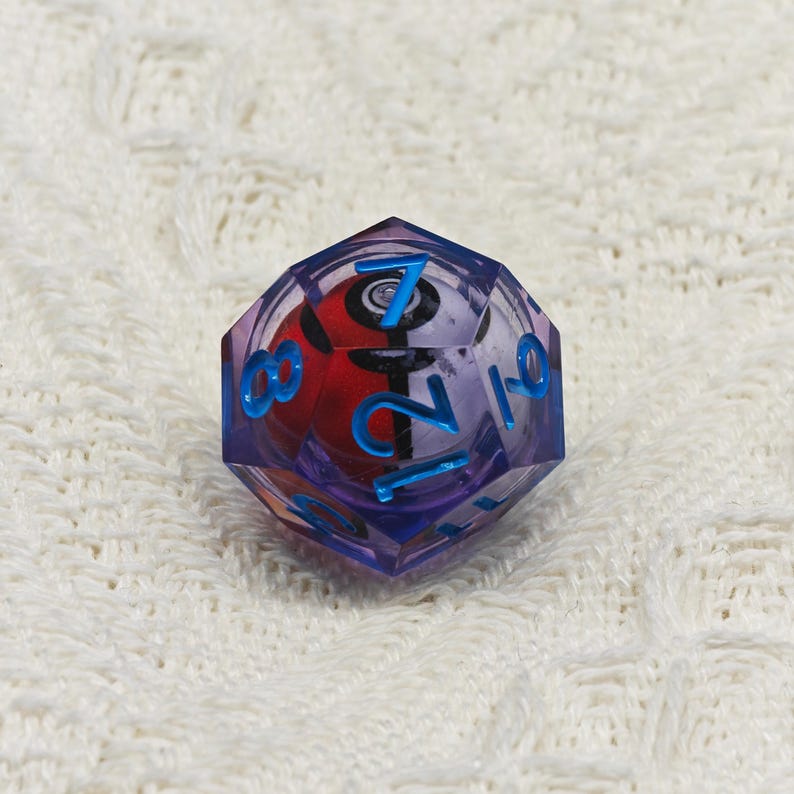 May include: A purple and blue 12-sided die with a Pokeball design and numbers 1 through 12 on the faces.