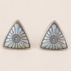 May include: A pair of triangular stud earrings featuring a silver frame and a central inlay of iridescent mother-of-pearl. The inlay is carved into a radial sunburst or flower petal pattern with a small circular center, set within a smooth silver border.
