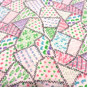 May include: A patchwork quilt featuring a variety of pastel-colored fabric pieces. The quilt showcases a mix of patterns, including hearts, stripes, and floral designs, all stitched together with black thread. The overall design is a mix of pink, green, blue, and purple.