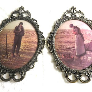 May include: Two vintage oval framed prints. Each print features a pastoral scene with figures in a field. The frames are ornate with a dark bronze finish. One print shows a man with a pitchfork, the other a woman with a basket.