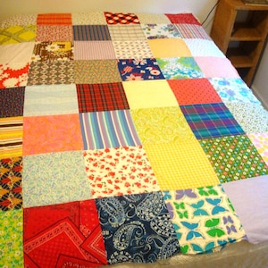 May include: A patchwork quilt featuring a grid of square fabric panels in various colors and patterns, including floral, paisley, plaid, striped, butterfly, and geometric prints in shades of red, yellow, blue, green, orange, and white.