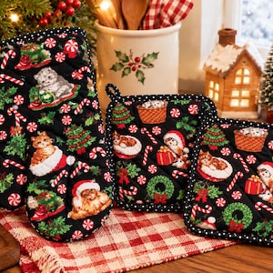 May include: A black quilted oven mitt and two square pot holders featuring a repeating Christmas print of cats, candy canes, holly, wreaths, and presents. The fabric has a black background with white polka dot trim along the edges.