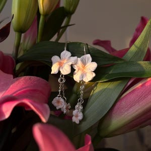 May include: A pair of silver dangle earrings with delicate white flower charms. The earrings feature two larger flowers at the top and two smaller flowers dangling below.