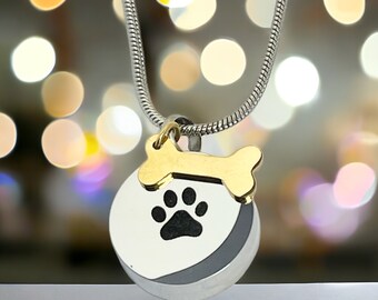 May include: Silver chain necklace with a round pendant featuring a black paw print and a gold bone charm.