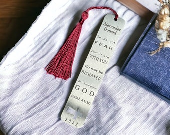 May include: A silver bookmark with a red tassel. The bookmark has the text "Alexander Donald" and a bible verse: "So do not fear for I am with you. Do not be dismayed for I am your God. Isaiah 41:10". The bookmark also has the year "2023" printed on it.