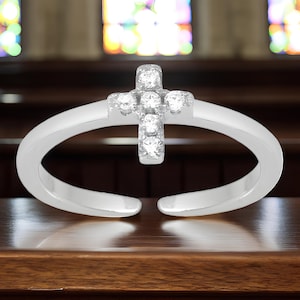 May include: A silver toe ring with a small, clear crystal cross design.