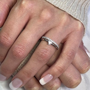 Può includere: Un delicato anello d'argento con un piccolo diamante a forma di cuore e una fascia di diamanti più piccoli.