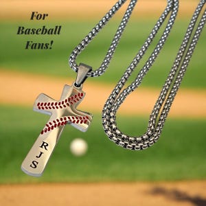 Peut inclure: Un collier en chaîne argentée avec un pendentif en forme de croix argentée. La croix est conçue pour ressembler à un ballon de baseball avec des coutures rouges. La croix porte les initiales "RJS" gravées.