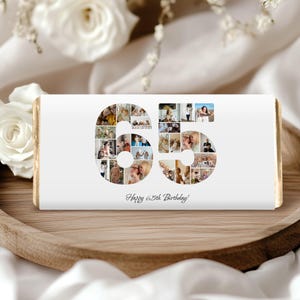May include: A rectangular chocolate bar wrapper featuring a white background with the number 65 formed by a collage of various small photographs. Below the number, the text Happy 65th Birthday is printed in a black cursive script font.