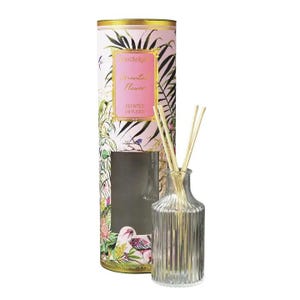 May include: A clear, ribbed glass reed diffuser bottle with several wooden reeds, accompanied by a tall, cylindrical cardboard packaging tube featuring a pink background, tropical leaf illustrations, and the text Candlelight Oriental Flower.